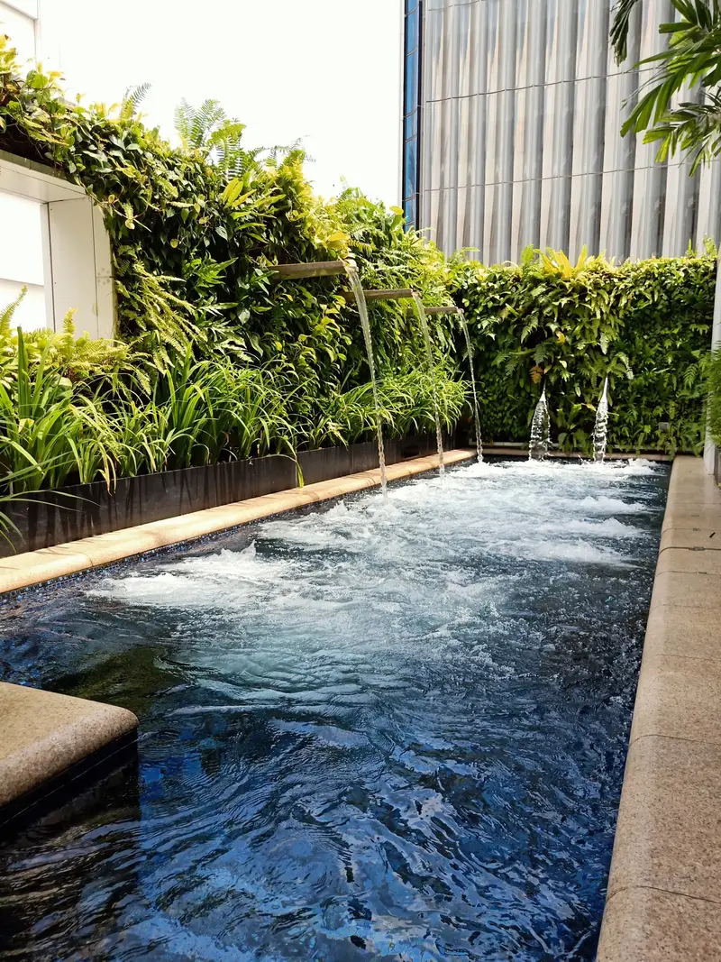 Crystal-clear plunge pool with waterfall spouts against a lush green wall