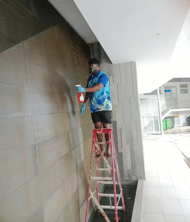 Technician cleaning a tiled wall from a ladder