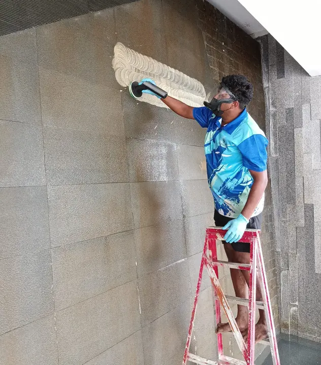 Technician scrubbing a tiled wall with a long brush
