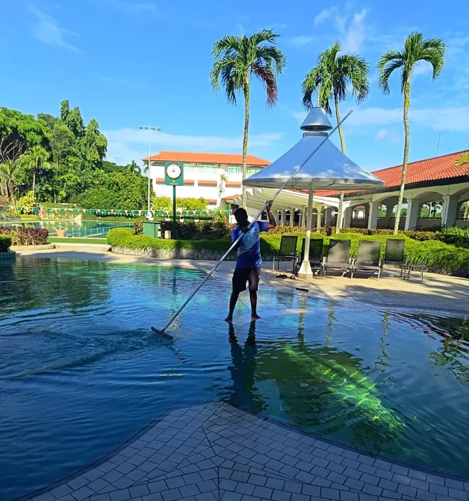 Technician using a pool skimmer in a large outdoor pool