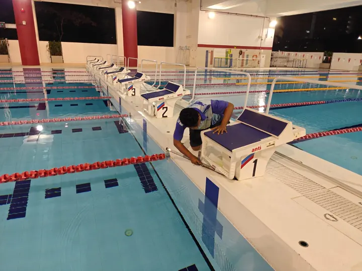 Technician cleaning starting blocks at an indoor pool