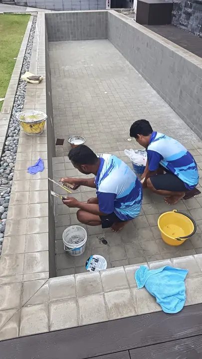 Technicians repairing tiles along an empty pool edge